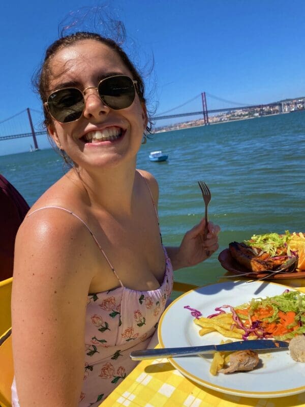 smiling woman with plate of food and holding a fork near the ocean
