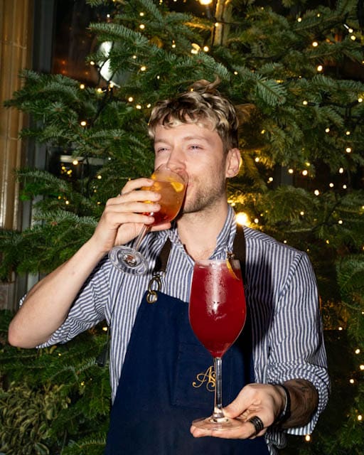 man holding cocktail beside christmas tree