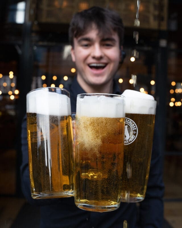 man holding three beers glasses and smiling