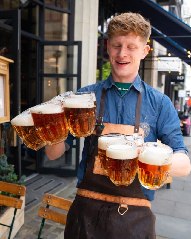 blond waiter holding eight glasses of beer