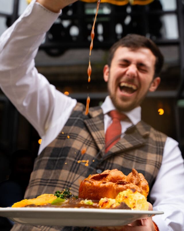 waiter pouring gravy over a plate of sunday roast