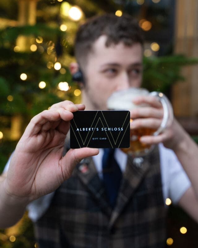 man dinking beer and holding an albert's schloss gift card